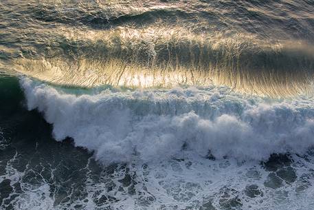 The sun at sunset, illuminates the waves crashing against the cliffs of Capo Nieddu