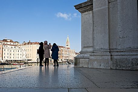 Turists take pictures of the bell tower of San Marco from the churchyard of the Basilica of the Madonna della Salute in the Dorsoduro district of Venice, Italy, Europe