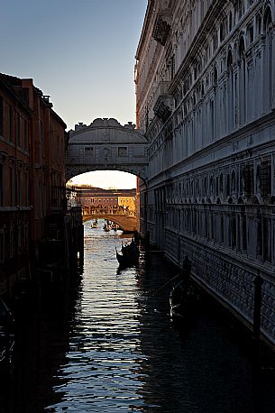 Gondoliers on the Rio di Palazzo show tourists the famous Bridge of Sighs or Ponte dei Sospiri, in the background illuminated by the morning light the Ponte della Paglia. Venice, Italy, Europe