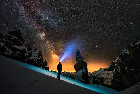 A hiker at night, wearing a head torch with in the background the famous Campanile di Val Montanaia