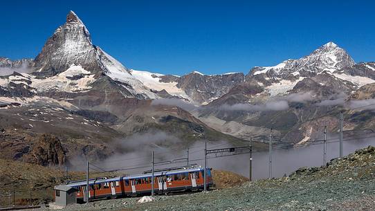 Train of Gornergrat railway arriving at the summit station, in the background  the magnificent Cervino or Matterhorn mountain peak, Zermatt, Valais, Switzerland, Europe