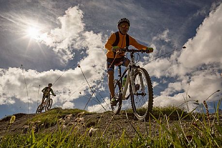 Two young mountain bikers come down from Biscia summit, in the background the Sesto Dolomites, Cadore, Italy