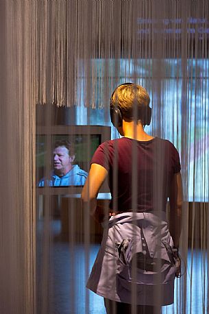 Young woman looks at and listens to audioguide   at museum of Swiss National Park in Zernez, Engadin, canton of Grisons, Switzerland, Europe