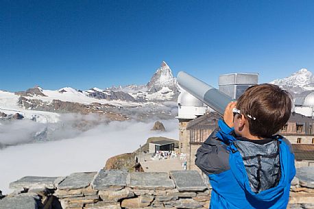 Child in the top of Gornergrat admiring the Matterhorn or Cervino mountain peak with a coin operated binoculars, Zermatt, Valis, Switzerland, Europe