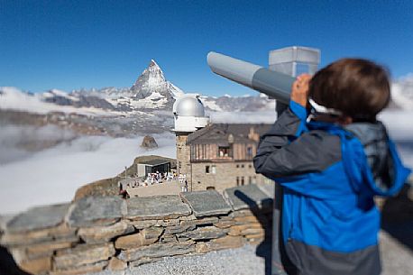 Child in the top of Gornergrat admiring the Matterhorn or Cervino mountain peak with a coin operated binoculars, Zermatt, Valis, Switzerland, Europe