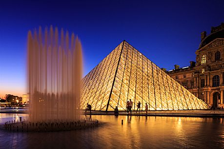 Silhouettes of tourist at sunset lights at the Louvre square with the glass pyramid and the fountain, Paris, France, Europe