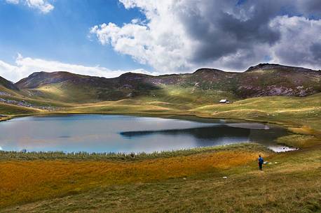 Hiker admires the quiet water of Fosses lake in the dolomites, Cortina d'Ampezzo, Veneto, Italy